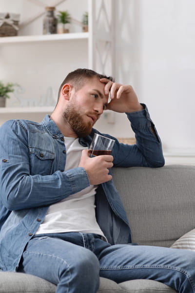 Мужчина сидит на диване со стаканом алкоголя